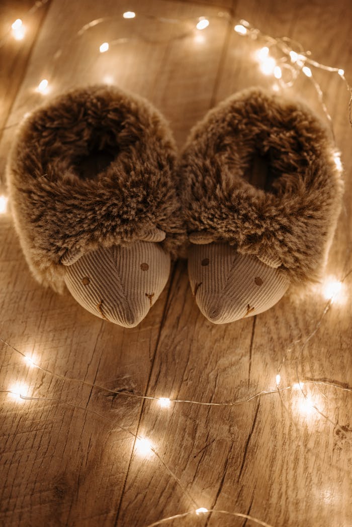 Pair of hedgehog-themed slippers surrounded by warm fairy lights on a wooden floor.